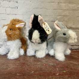 Three plush bunny figurines sit on a wooden surface.