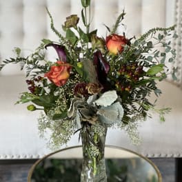 Tall mixed bouquet in a clear glass vase with orange roses and dark calla lilies