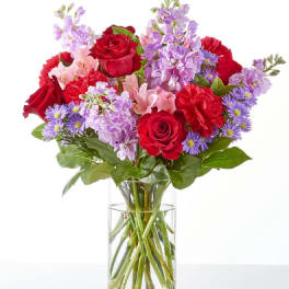 Bouquet of red roses, pink lilies, and purple flowers in a clear glass vase