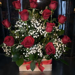 Red roses arranged with white baby's breath in a wooden box tied with a red ribbon