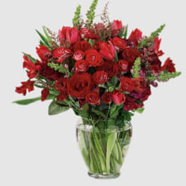 Red roses and tulips arranged in a clear glass vase
