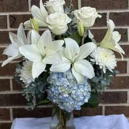 White lilies and roses with blue hydrangea in a glass vase