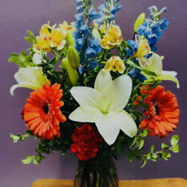 Mixed bouquet with white lilies, orange gerbera daisies, blue flowers, and red carnations in a vase