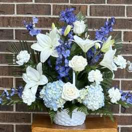 White lilies and roses with blue flowers in a white basket