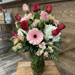 Bouquet of red and pink roses with a pink gerbera daisy in a glass vase