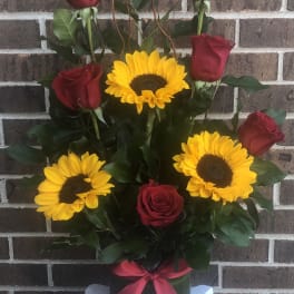 Red roses and yellow sunflowers in a vase with a pink ribbon