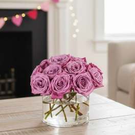 Low arrangement of mauve roses clustered in a clear glass vase on a table