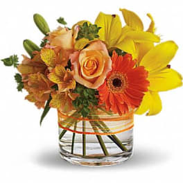 Low glass vase arrangement with yellow lilies, orange gerbera daisies and peach roses
