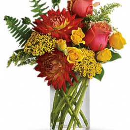 Warm arrangement of red dahlias and yellow and pink roses in a clear glass cylinder vase