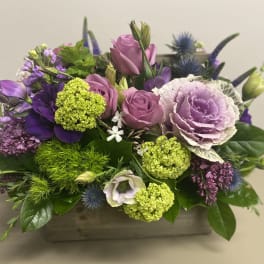 Low centerpiece of lavender roses, ornamental cabbage, green blooms and purple flowers in a wooden box