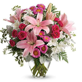 Pink lilies and roses in a clear glass vase with white and magenta flowers