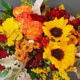 Bouquet of yellow sunflowers, orange and red roses, and orange mums with silvery foliage.