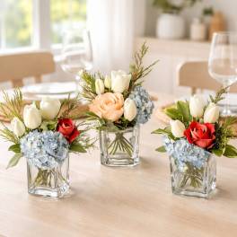 Three small floral centerpieces in glass cubes with tulips, roses, and hydrangeas