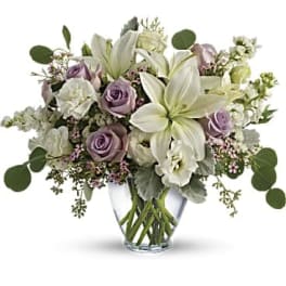 Arrangement of white lilies and pale lavender roses in a clear glass vase