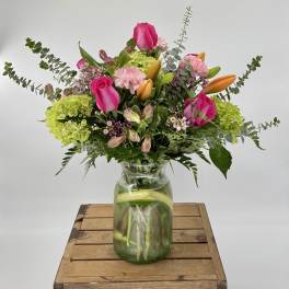 Mixed bouquet of pink roses, orange lilies, and green hydrangeas in a clear glass jar vase
