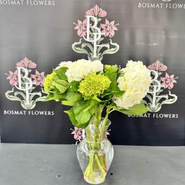 White hydrangeas and green blooms in a clear glass vase
