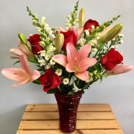 Bouquet of pink lilies and red roses in a red glass vase