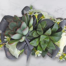 Succulent arrangement with white flowers and dark ribbon on a light surface
