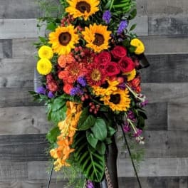 Tall standing spray of sunflowers, red roses, and bright mixed flowers on a metal easel.