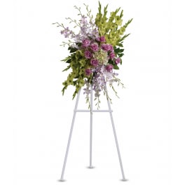 Tall standing spray of lavender roses, white orchids, and green flowers on a white easel.