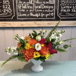 Colorful flower arrangement in a white pedestal vase with a butterfly accent