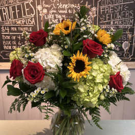 Bouquet of red roses, sunflowers, and hydrangeas in a glass vase