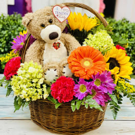 Basket arrangement with a teddy bear surrounded by colorful flowers