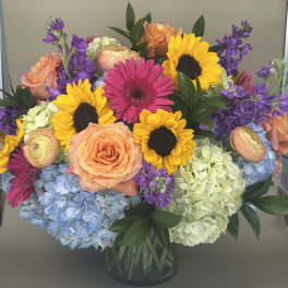 Colorful bouquet with sunflowers, roses, gerbera daisies, and hydrangeas in a glass vase