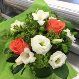 Coral and white roses arranged in a green container with white blooms and greenery.