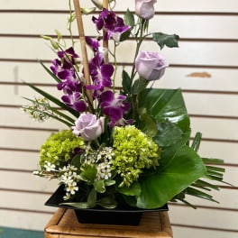 Purple orchids and pale lavender roses in a black vase