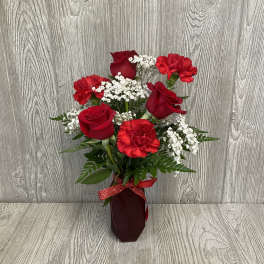 Red roses and carnations in a burgundy vase with a ribbon