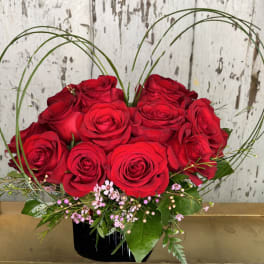 Red roses arranged in a black vase with arched grass accents