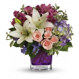 Bouquet of white lilies, pink roses, and purple flowers in a purple glass vase