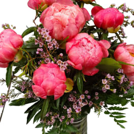 Pink peonies arranged in a glass vase with small purple filler flowers