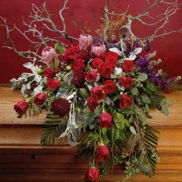 Large floral arrangement with red roses and pink protea on a wooden table