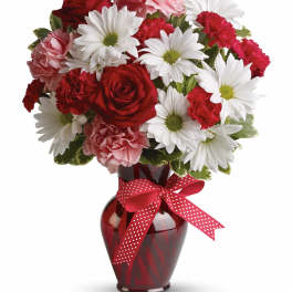 Red roses, white daisies, and pink carnations in a red vase with a ribbon