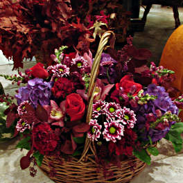 Basket arrangement of red, purple, and white flowers with pumpkins nearby