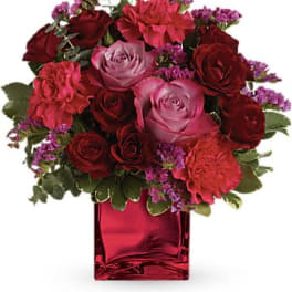 Compact bouquet of red and pink flowers in a red glass cube vase