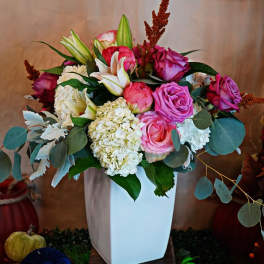 Tall white vase of pink roses, white hydrangeas, and lilies in a mixed arrangement