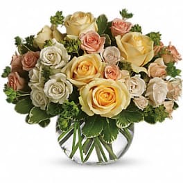 Round arrangement of cream, peach, and yellow roses in a clear glass bowl vase