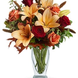 Autumn-toned bouquet of orange lilies and red roses in a clear glass vase