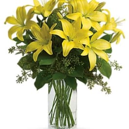 Tall bouquet of yellow lilies in a clear glass rectangular vase
