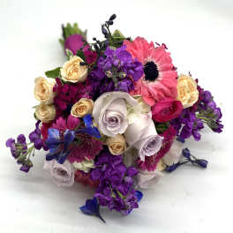 Hand-tied bouquet of purple stock, pink gerbera daisies, roses, and blue delphinium.