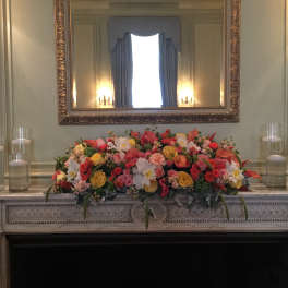 Colorful floral arrangement on a mantel with glass candles on both sides