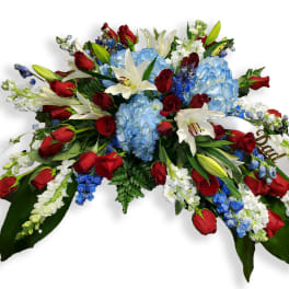 Casket spray with red roses, blue hydrangeas, and white lilies
