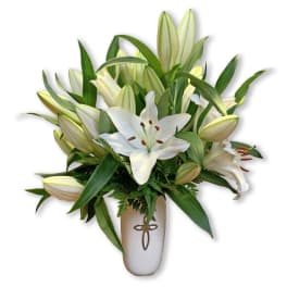 White lilies arranged in a tall vase with green foliage