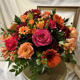 Mixed bouquet of roses, gerbera daisies, and carnations in warm pink, orange, and red tones