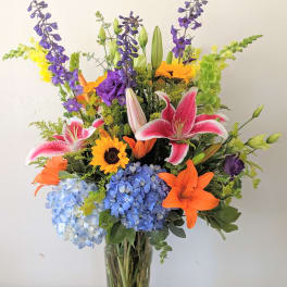 Colorful mixed bouquet in a clear glass vase with lilies, hydrangeas, and sunflowers