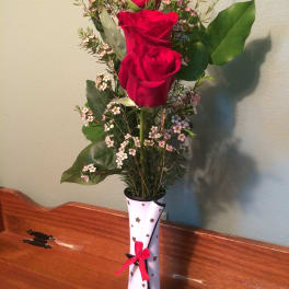 Three red roses in a decorated vase with small pink filler flowers