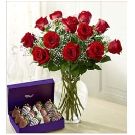 Red roses in a glass vase beside a box of chocolate-covered strawberries